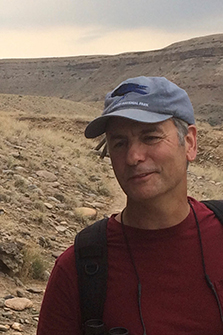 Photo of Josh Rosenthal wearing a hat and red shirt and backpack