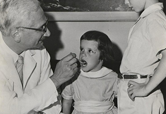Black and white photo of Dr. Albert Sabin giving polio vaccine to a young child
