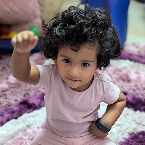 Photo of young Bangladeshi girl with her hand raised up, wearing a sleep monitor bracelet