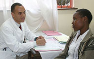Dr. Gerald Bloomfield speaks to young male patient, both seated, a table covered with papers between them