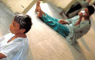 PHOTO: A man up close seated on the floor stares off camera; one in the background, out of focus, also seated on the floor
