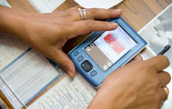 Close up of hands holding PDA displaying data, on top of papers and desk