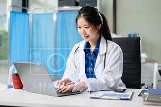 A young female doctor wearing a white lab coat and a stethescrope is working on a laptop in a medical office. She is smiling while interacting with a futuristic, holographic interface displaying medical and scientific icons. The background features blue hospital curtains and a clinical setting, with a tablet and coffee cup on the desk.