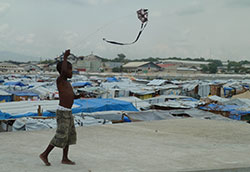 Photo courtesy of CDC, CC BY 2.0, Boy flies a kite, refugee camp in background, after 2010 earthquake in Haiti