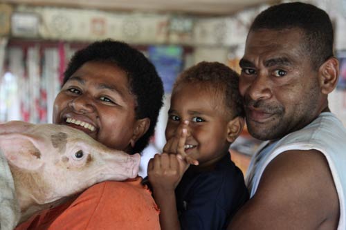 Small pig rests head on woman’s shoulder, child and man stand behind woman