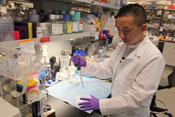 Japanese fellow Dr. Atsushi Tanaka in lab full of materials, wearing white lab coat