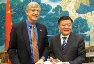 Dr Francis Collins and China health minister Chen Zhu stand side by side, smiling for camera, each holding a gift