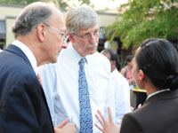 Dr Roger Glass and Dr Francis Collins listen attentively to woman speaking, her back to the camera, outdoors