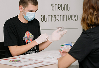 A person in a mask puts on gloves as they talk with a woman at an HIV testing clinic in Tblisi, Georgia