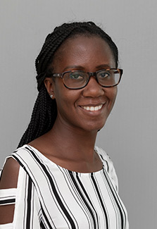 In this headshot of Dr. Anita Arinda, she wears glasses and a white blouse with black vertical  stripes