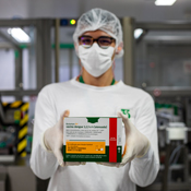 A research worker, wearing a hair net, face mask, and glasses, holding a Butantan Dengue vaccine