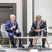 Photo of Dr. Steven Schiff (left) sitting in a chair and speaking into a microphone and Dr. Jay Bhattacharya, sitting in a chair and holding a microphone, listening to Dr. Schiff.