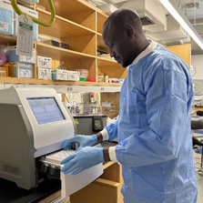 Dr. Amadou Niangaly wears blue protective gear and gloves as he works in a laboratory.