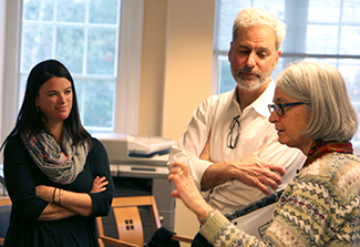 In this photo, Flora Katz informally speaks with Rachel Sturke and Josh Rosenthal in a Fogarty International Center office. Gesturing as she speaks, Flora is wearing a brown and grey sweater, Rachel is attired all in black with a gray scarf, and Josh is dressed in a white shirt. 