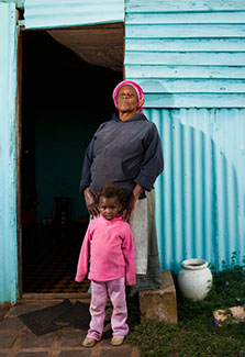 African mother and young daughter stand in front of their home