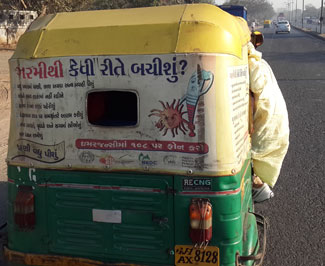 Back of an auto rickshaw on a street in India, advertisement on back includes public health message on extreme heat
