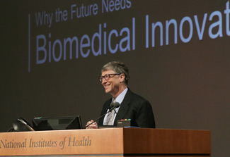 Bill Gates, smiling, stands at podium, podium reads National Institutes of Health, slide projected in background