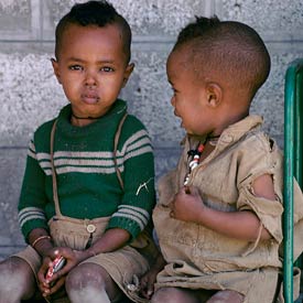 Two young boys seated, one looks at camera with swollen infected eye