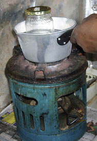 Pan of water, containing small jar with lid, being heated over small stove