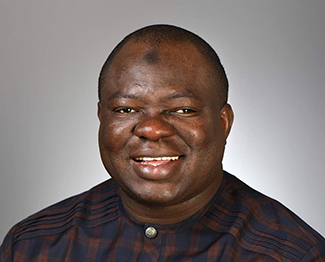 This photo shows Dr. Azeez Butali smiling and wearing a dark blue and brown plaid shirt