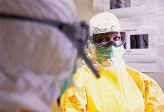 2 medical workers wearing personal protective equipment in the CDC mock Ebola treatment unit observe each other