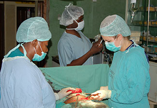 Three medical workers in scrubs opearting on a patient in Zambia