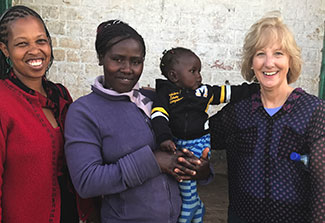 Dr. Debra Litzelman pictured with two women, one holding a baby, at a research site in Kenya