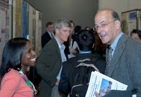 Young woman stands smiling, facing Fogarty Dir Roger Glass during busy poster session