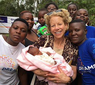 NICHD Director Dr. Diana Bianchi, center holding a baby, surrounded by young people in Kenya
