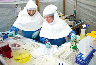 Two workers in personal protective gear test samples and record data in makeshift lab with tarp walls