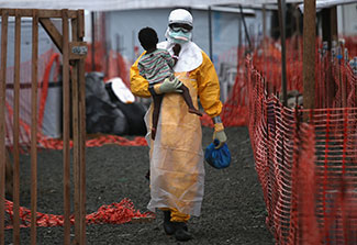 Health worker in personal protective equipment carries a child suspected of having Ebola in treatment center