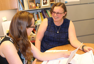 Dr Emily Vogtmann and another female researcher seated at a table in an office review and discusses data printed on paper