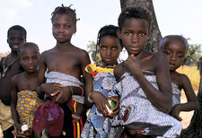 Group of young African children gather to look at camera, some children carry younger children wrapped on their backs