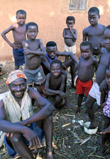 Group of young African children gather, ground littered with husks, one man seated on ground in front of boys