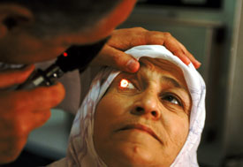 Older woman looks up, medical worker holds up her eyelid and uses instrument to shine light in her eye