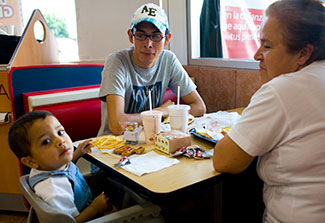 An older woman, teenage boy and young child in high chair eat a meal at a fast food restaurat