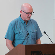 This photo shows Patrick Duffy of NIAID standing at a podium. He is wearing glasses and a light blue shirt.