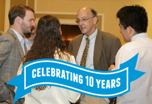 Fogarty Director Roger Glass speaks with Fogarty fellow and scholars, ribbon reads celebrating 10 years