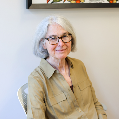 Dr. Flora Katz, wearing dark rimmed glasses and a loosely fitted khaki blouse, relaxes in her office at Fogarty.