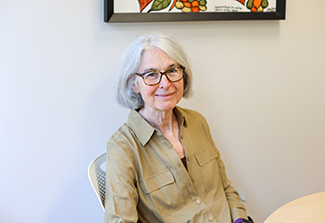 Dr. Flora Katz, wearing dark rimmed glasses and a loosely fitted khaki blouse, relaxes in her office at Fogarty.