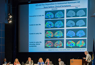 Richard Hodes speaking at a podium in auditorium, slide of brain images projected, panel of 6 researchers seated on stage
