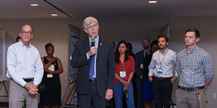 Dr Francis Collins holding microphone speaks to crowd of Fellows and Scholars during orientation, stands next to Dr Roger Glass