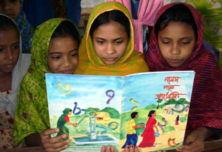 A group of young girls in Bangladesh reads a book together, illustrated book cover shows people pumping and carrying water