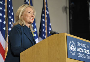 Secretary of State Hillary Clinton smiles from a podium with NIH logo, American flags in background