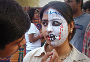 Young Indian woman receives face painting from may, half of face covered with white makeup, fake cigarette, reads no smoking
