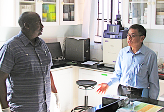 This photo shows Charles Wood (right) talking with a mentee (left). They are standing in a lab behind a table with a lap top on it.