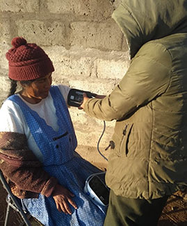Health worker heavy coat takes the blood pressure of a seated woman.