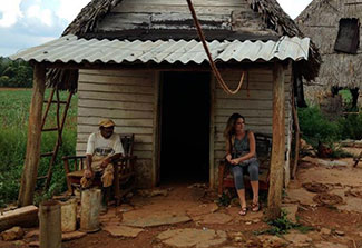 Older man and younger student seated in front of small farm house in Cuba