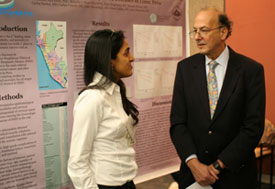Woman speaks with Dr Roger I Glass in front of large poster displayed in conference room