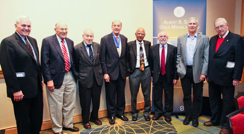 Eight men, all previous Sabin gold medal winners, pose in a row for the camera, with Roger Glass in the middle